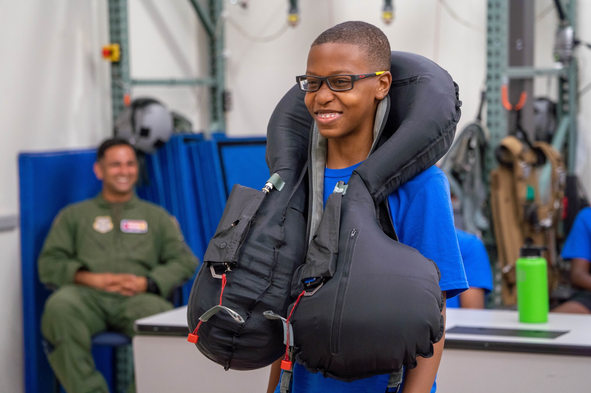 A member from the Organization of Black Aerospace Professionals Aerospace Career Education Academy dons a life jacket during a brief on safety equipment outfitted in different aircraft during a base tour at Joint Base Pearl Harbor-Hickam, Hawaii, July 28, 2022. OBAP was founded in 1976, and has since encouraged diversity in the avionics industry by supporting aspiring aviation professionals through a series of scholarships, mentoring, training and education programs. (U.S. Air Force photo by Senior Airman Makensie Cooper)