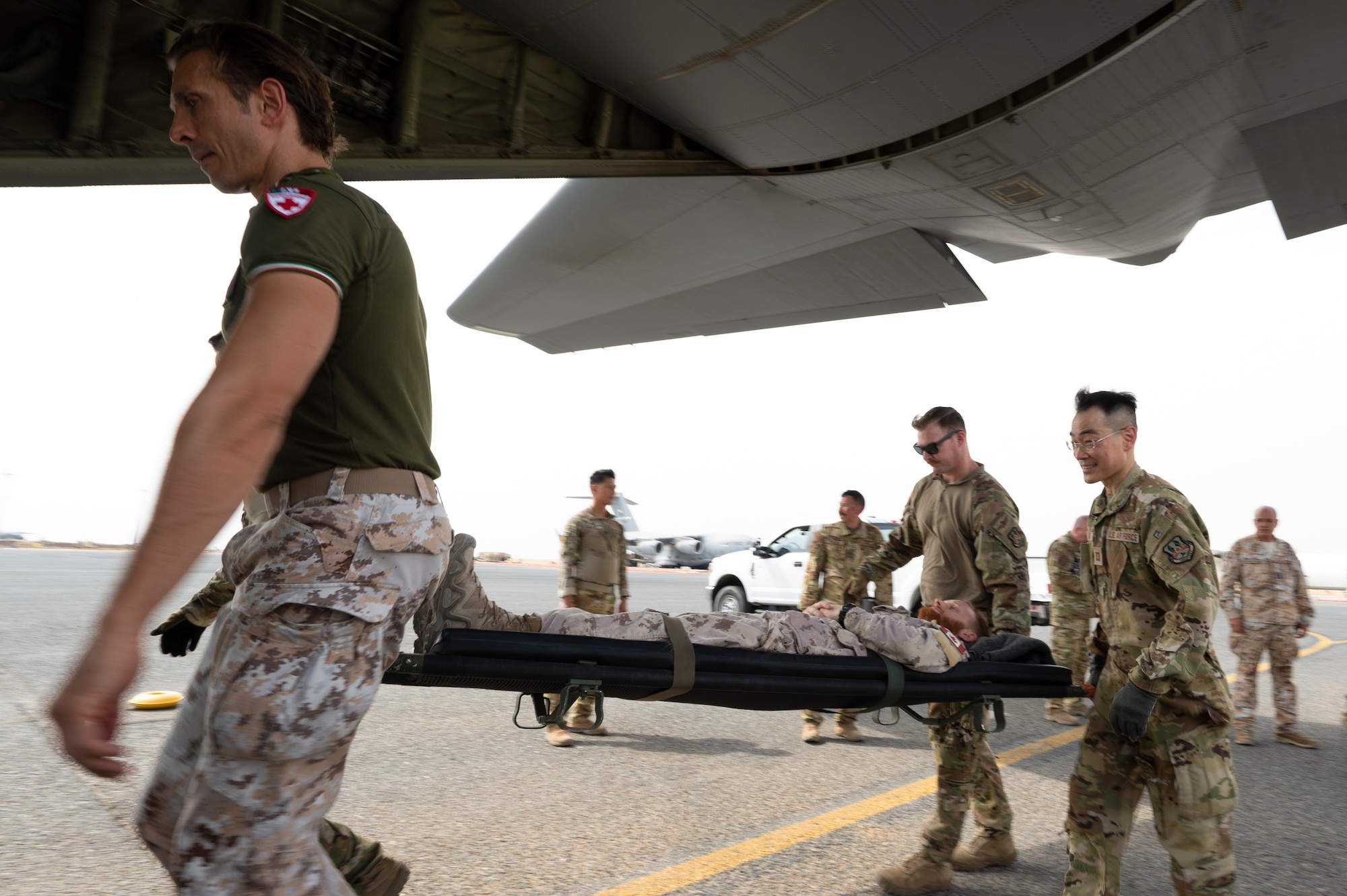 U.S. Air Force and Italian Air Force military personnel transport Capt. Stefan Sabo-Walsh, an infantry officer in the Canadian Armed Forces, as a mock patient during a coalition training exercise at Ali Al Salem Air Base, Kuwait, July 29, 2022. The training was able to dive into the specifics on how the 405th EAES tackles everything from establishing initial roles and responsibilities of each crew member and working hands-on with medical equipment, to responding to different aircraft emergency scenarios. (U.S. Air Force photo by Staff Sgt. Dalton Williams)