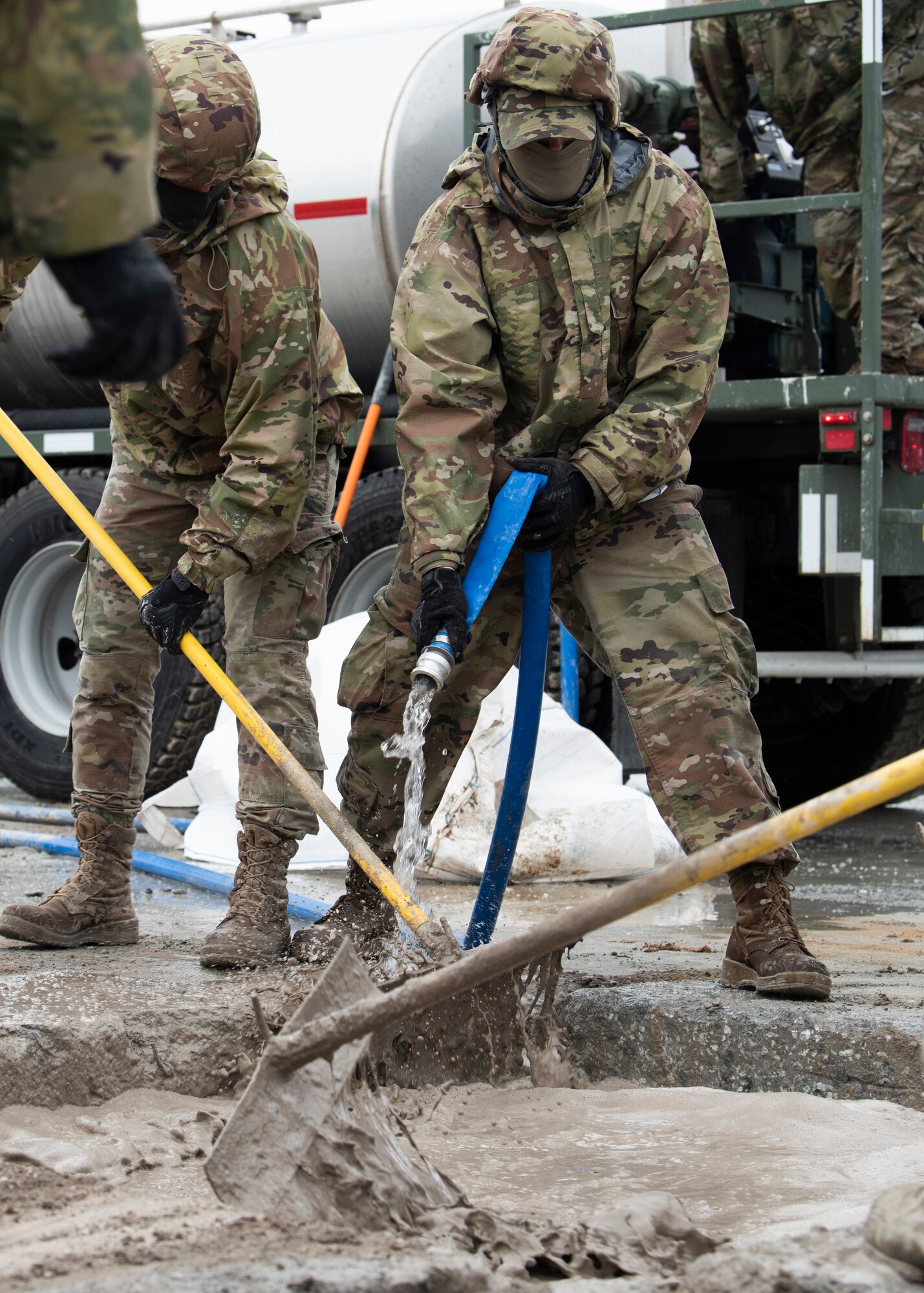 Personnel work outdoors in the rain to fill a crater with cement
