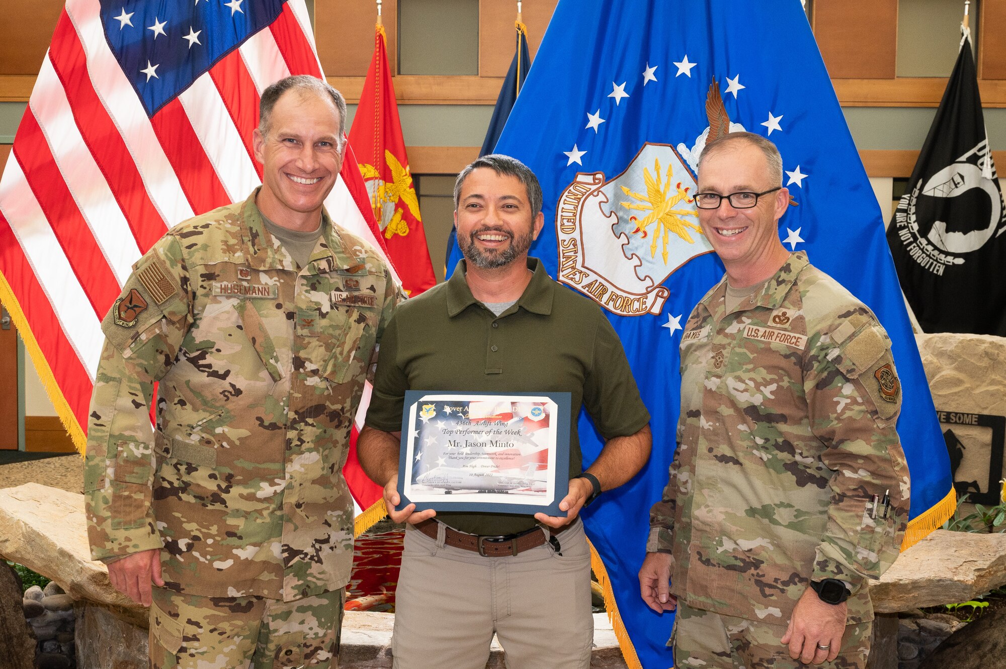 Col. Matt Husemann, left, 436th Airlift Wing commander, and Chief Master Sgt. Timothy Bayes, 436 AW command chief, present Jason Minto, Air Force Mortuary Affairs Operations multimedia specialist, with a certificate as the week’s top performer at Dover Air Force Base, Delaware, Aug. 10, 2022. Husemann and Bayes presented Minto with a certificate and coin for his outstanding performance. (U.S. Air Force photo by Mauricio Campino)