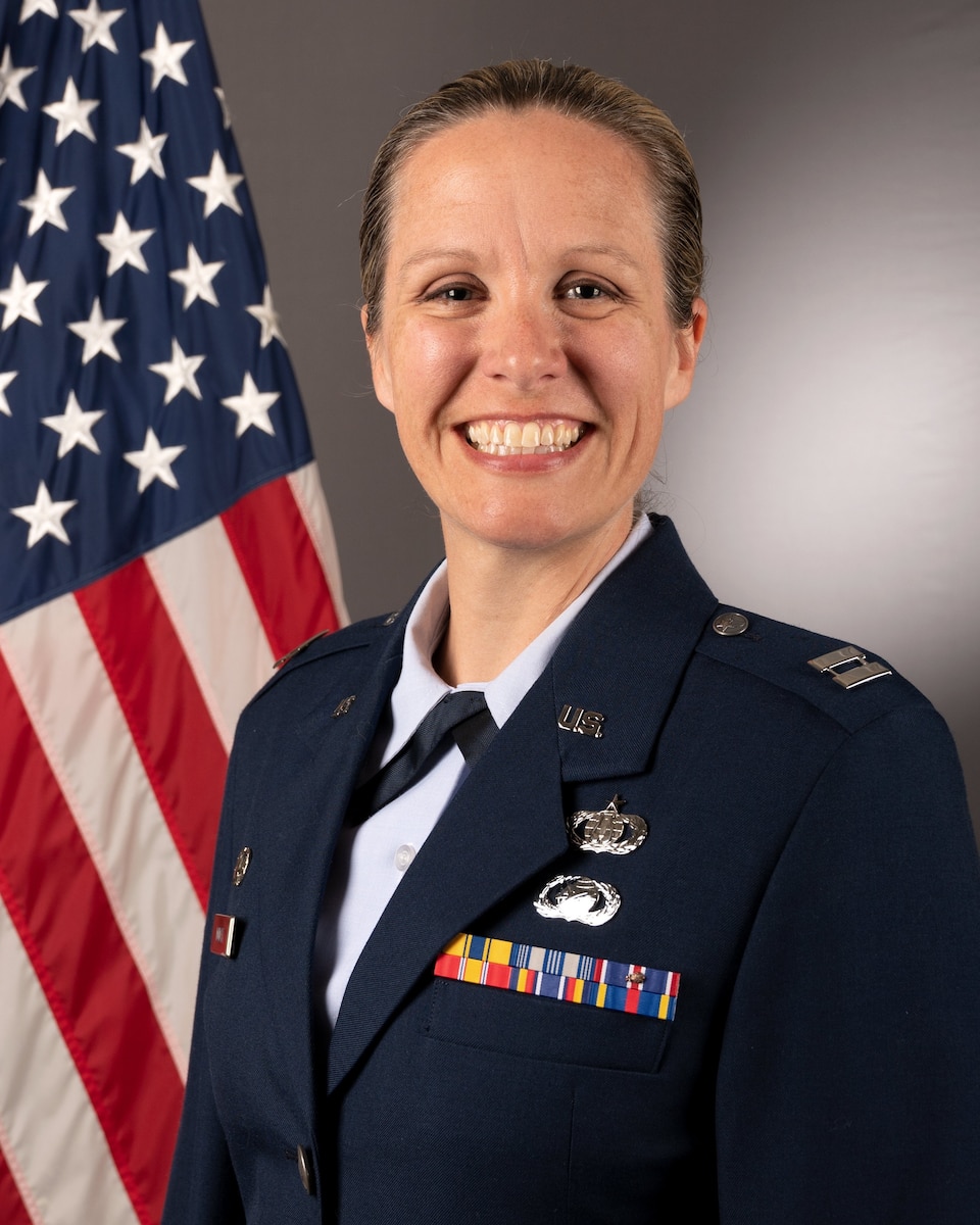 An official bio photo of Captain Christina Muncey in front of the American flag. She is wearing the blue service dress uniform.