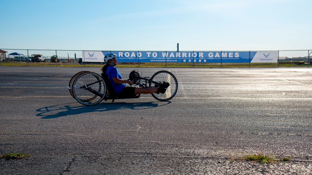 A hand cyclist passes a Road to the Warrior Games sign.