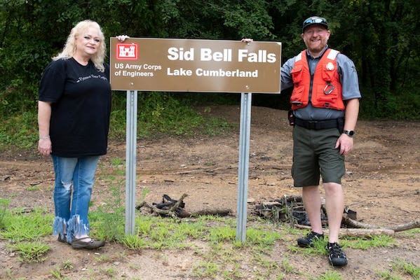 Lake Cumberland Resource Manager Jon Friedman and Stacey Bell pose Aug. 5, 2022, next to the new “Sid Bell Falls” sign on the shoreline of the lake in Watauga, Kentucky. The U.S. Army Corps of Engineers Nashville District officially named the landmark after her grandfather Sid Bell who owned the land and operated a gristmill before the Corps of Engineers purchased the property when constructing Wolf Creek Dam. (USACE Photo by Lee Roberts)