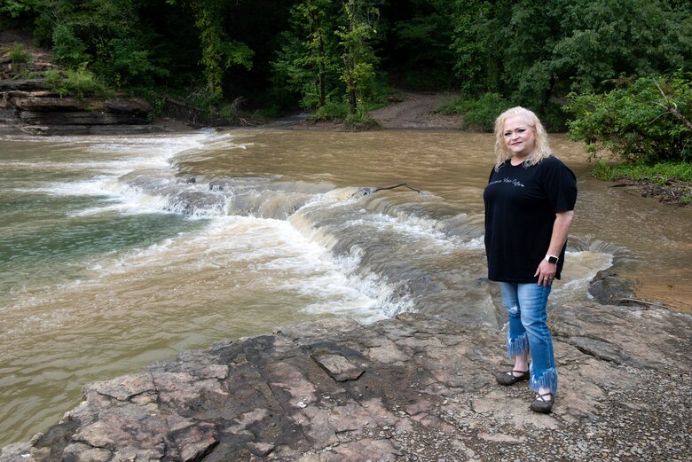 Stacey Bell stands next to “Sid Bell Falls” on the shoreline of Lake Cumberland Aug. 5, 2022, during a visit to the landmark in Watauga, Kentucky. Stacey is the granddaughter of Sid Bell. It was her idea to approach the Corps of Engineers about officially naming the falls. The naming also helps first responders with knowing where to go in case of emergencies. (USACE Photo by Lee Roberts)
