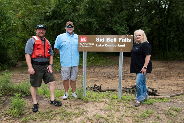 Lake Cumberland Resource Manager Jon Friedman (Left), Marina at Rowena General Manager David Dyson, and Stacey Bell pose Aug. 5, 2022, next to the new “Sid Bell Falls” sign on the shoreline of the lake in Watauga, Kentucky. The U.S. Army Corps of Engineers Nashville District officially named the landmark after Stacey’s grandfather Sid Bell who owned the land and operated a gristmill before the Corps of Engineers purchased the property when constructing Wolf Creek Dam. (USACE Photo by Lee Roberts)