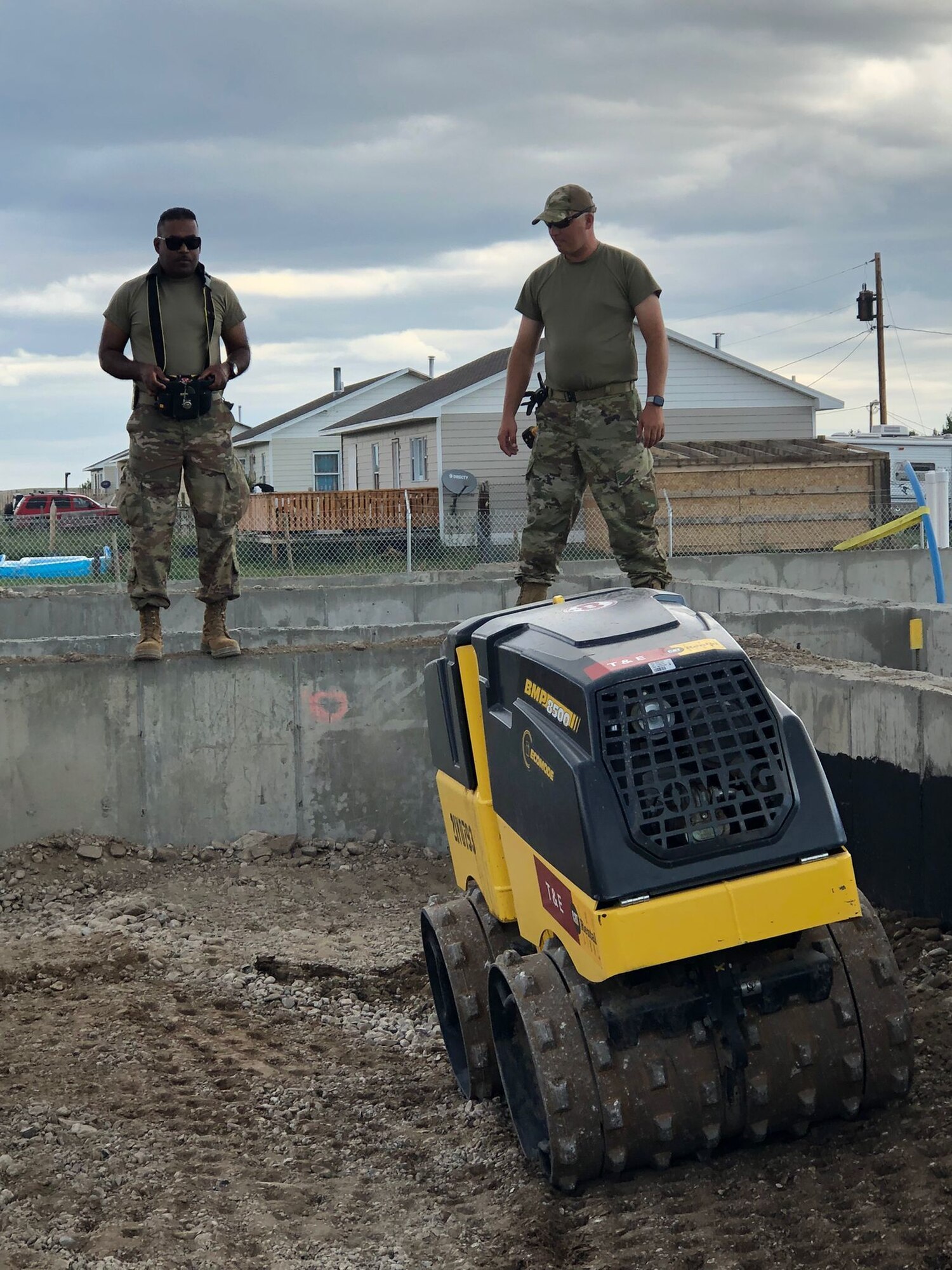 Two Airmen operating a remotely controlled piece of construction equipment outside.