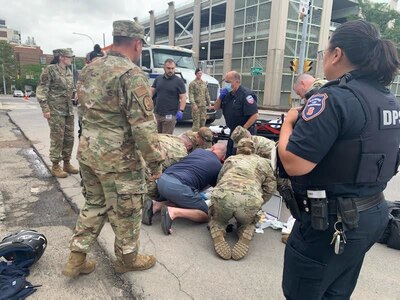 New York Air National Guardsmen and EMS provide emergency care to an unidentified man during a military conference Aug. 9, in Syracuse, NY. Airmen were returning from a break when they witnessed the man suffering from a grand mal seizure and consequential head wound on Waverly Ave.