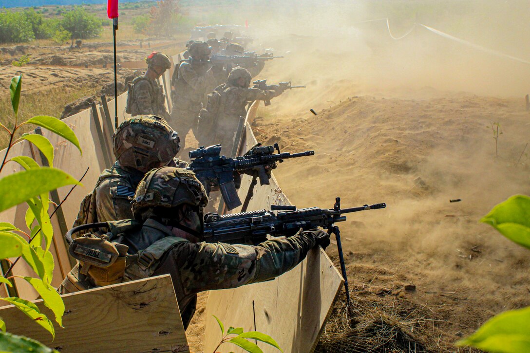 Soldiers standing in a trench fire weapons in a field.