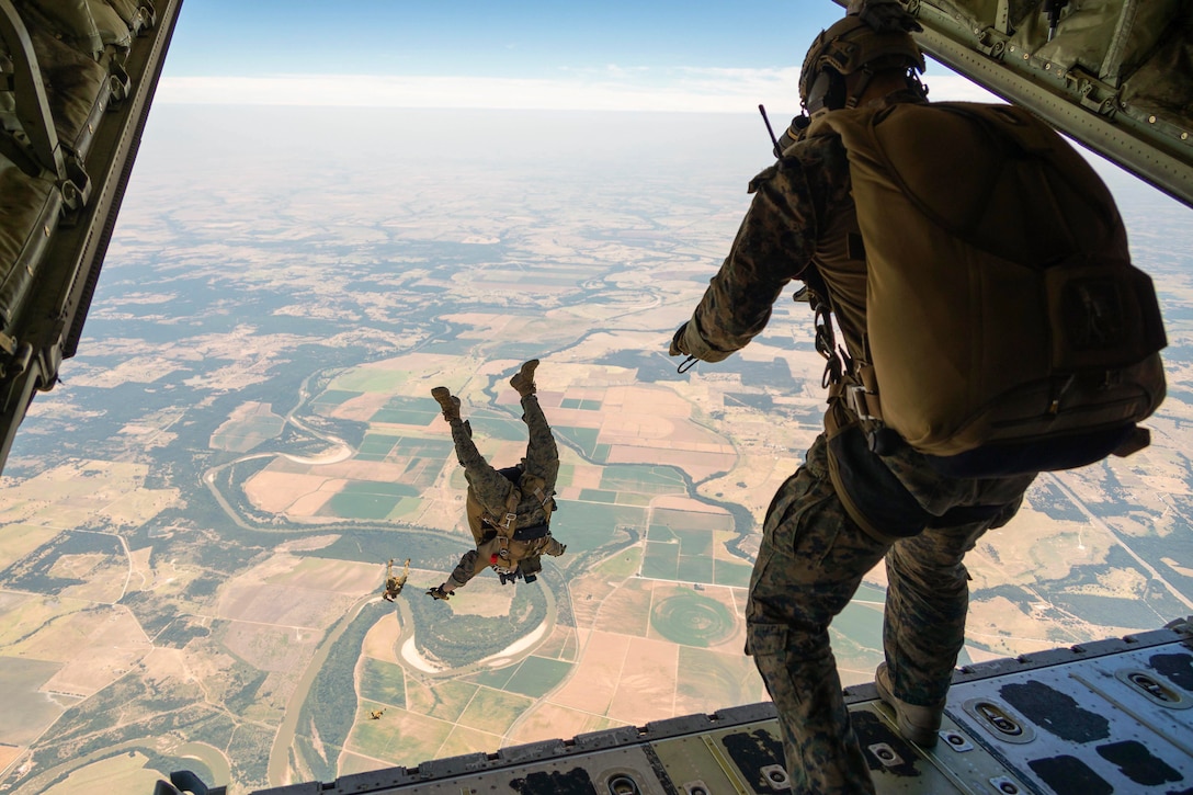 Three Marines jump out of an aircraft wearing parachutes.
