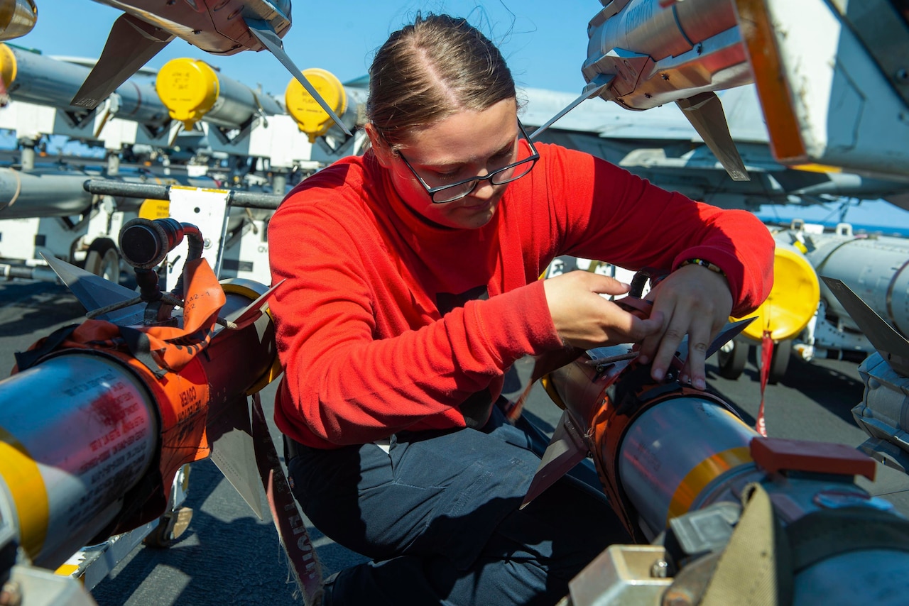 A sailor inspects missiles aboard a ship at sea.