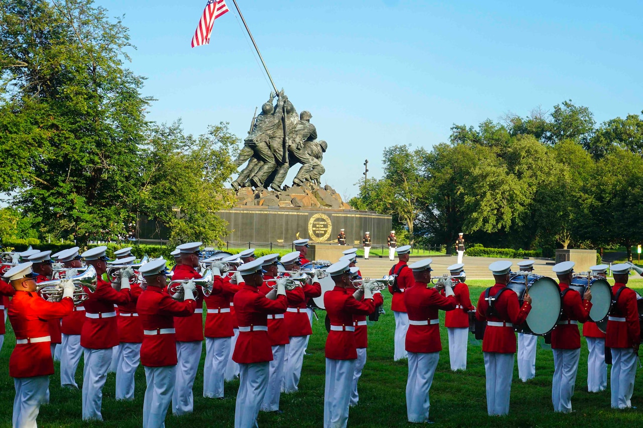 A Marine band performs with various instruments in front of a large statue.