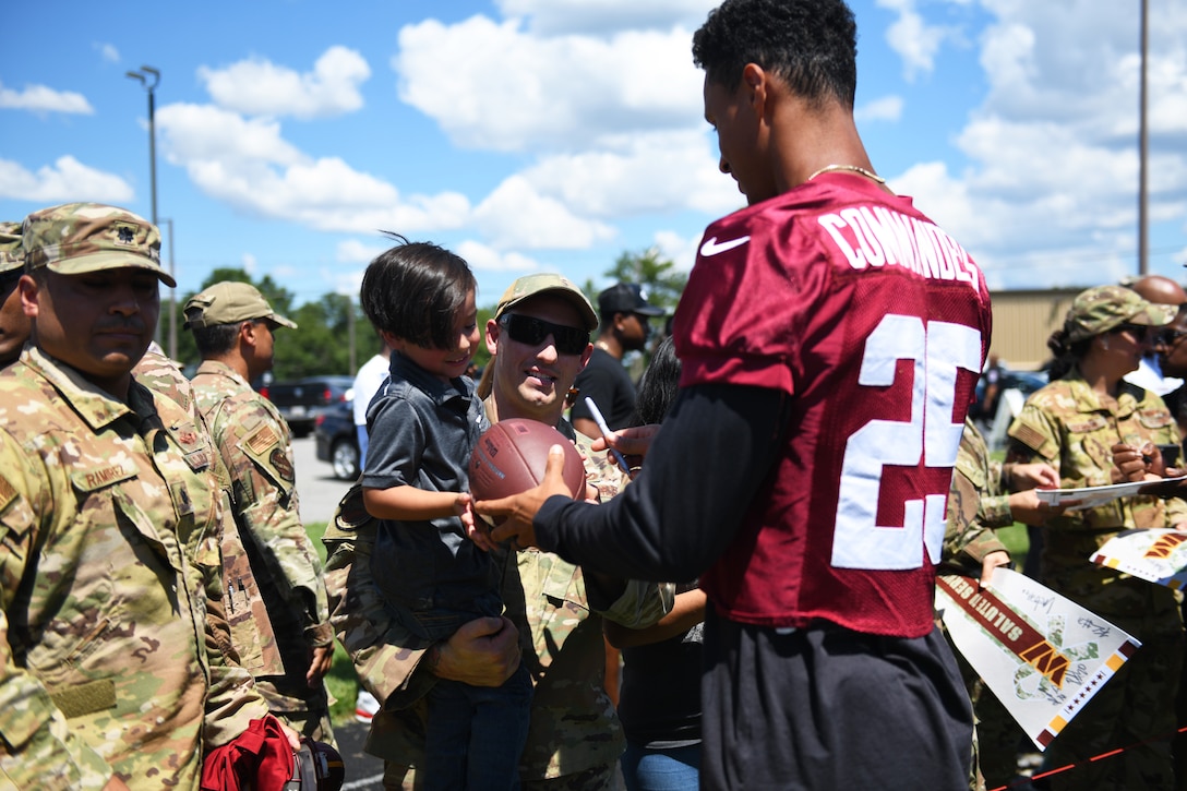 Benjamin St-Juste, Washington Commanders football team cornerback, signs a football for a service member's family during the meet and greet at the conclusion of their practice at Joint Base Andrews, Md., Aug. 12, 2022.