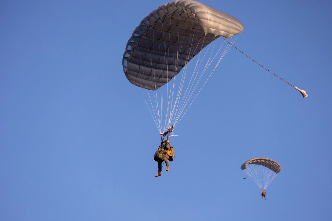 Two Marines free fall with parachutes next to each other.