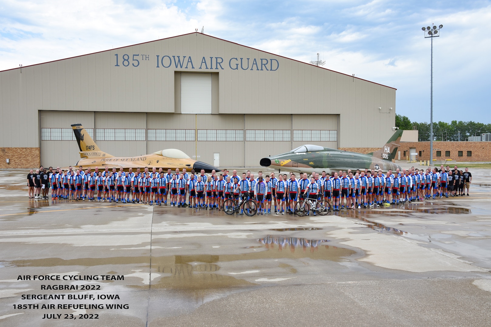 Group of people in cycling kit stand together for a photo in front of two jets