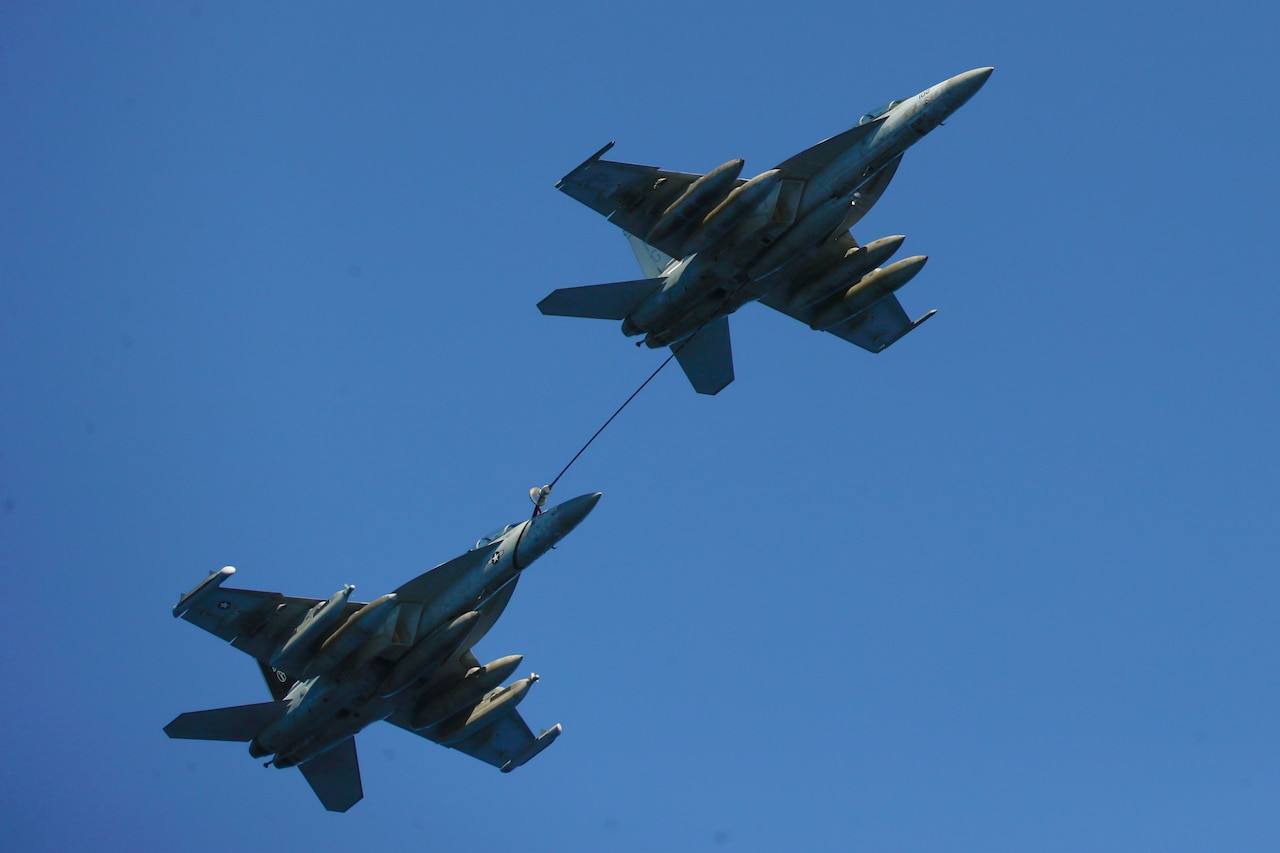 A boom from one jet extends to another as they fly in blue sky.