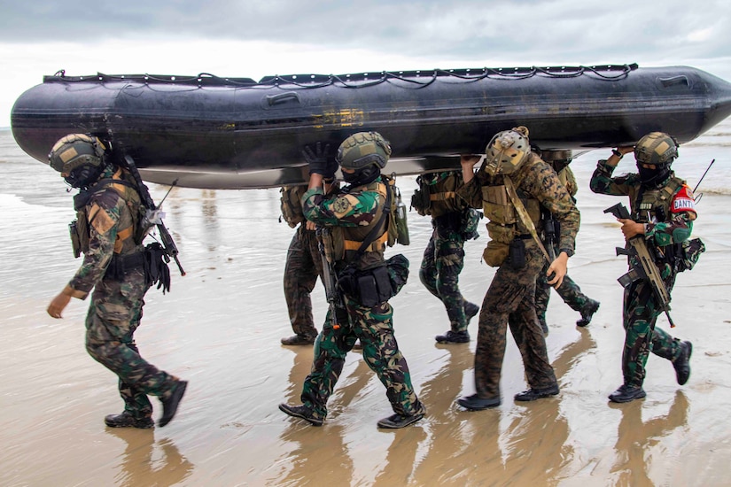 Marines carry a small inflatable boat on the beach.