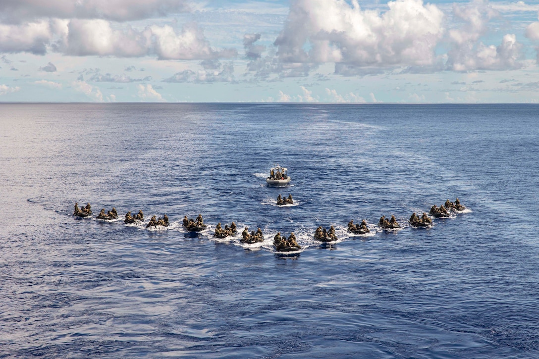 Marines in small boats move in formation in a body of water.