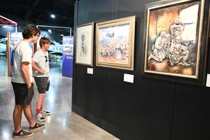 Two young men look at at a piece of artwork from the  Art Exhibit: Honor, Courage, Commitment: Marine Corps Art, 1975-2018.