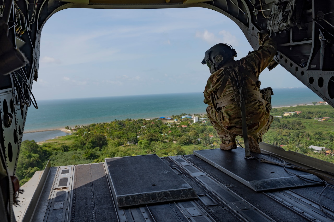 A soldier looks out from the back of a helicopter.