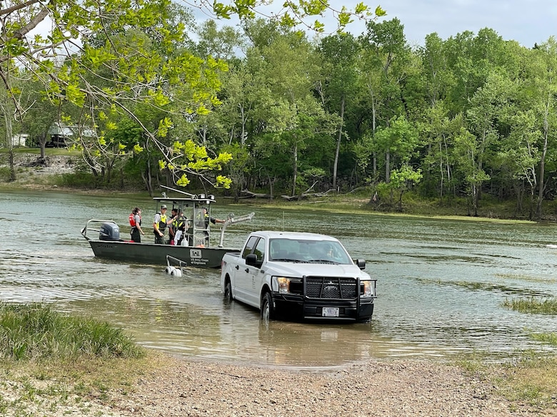 a park ranger truck loads a park ranger boat onto a boat trailer in a river