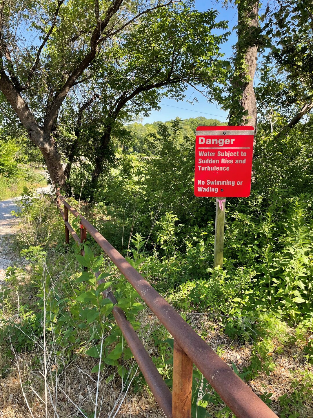 A warning sign along a road with metal rail barrier