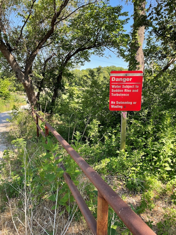 A warning sign along a road with metal rail barrier