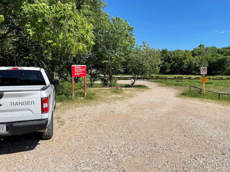 A park ranger truck is parked next to a warning sign by a river