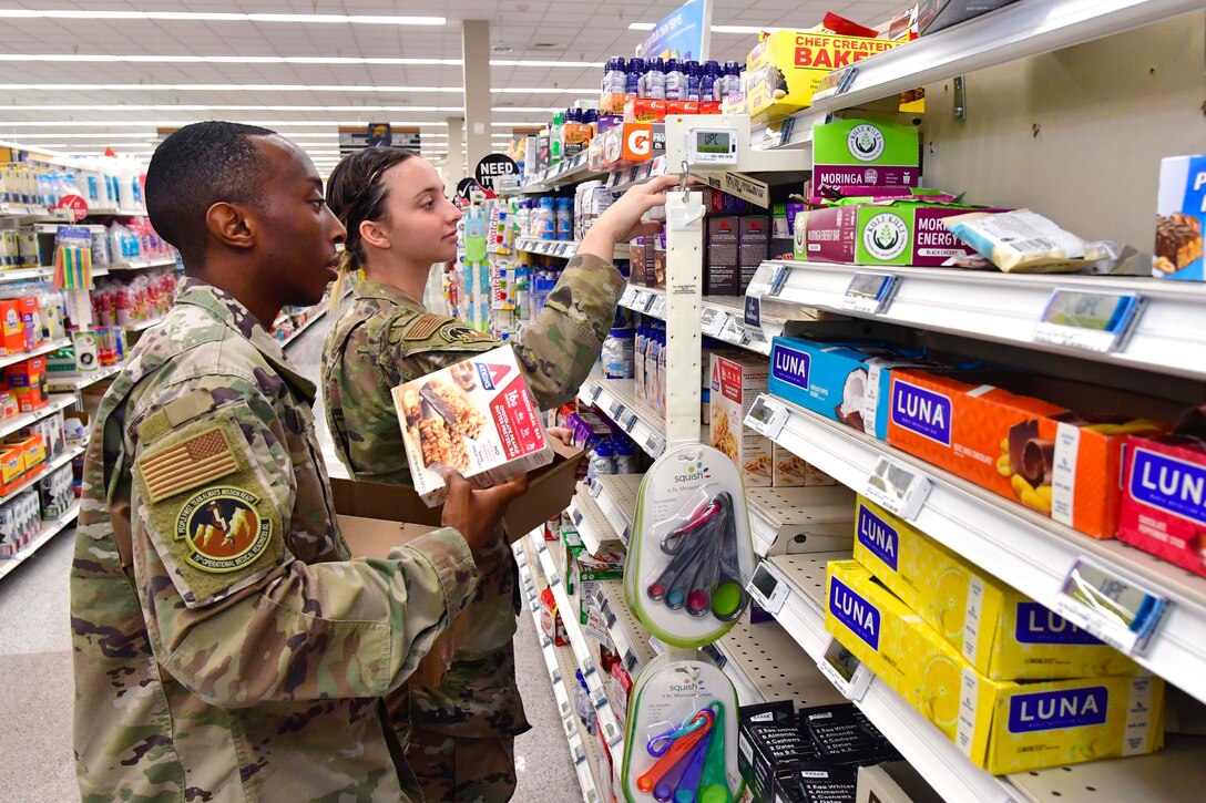 Two airmen stock items on a supermarket shelf.