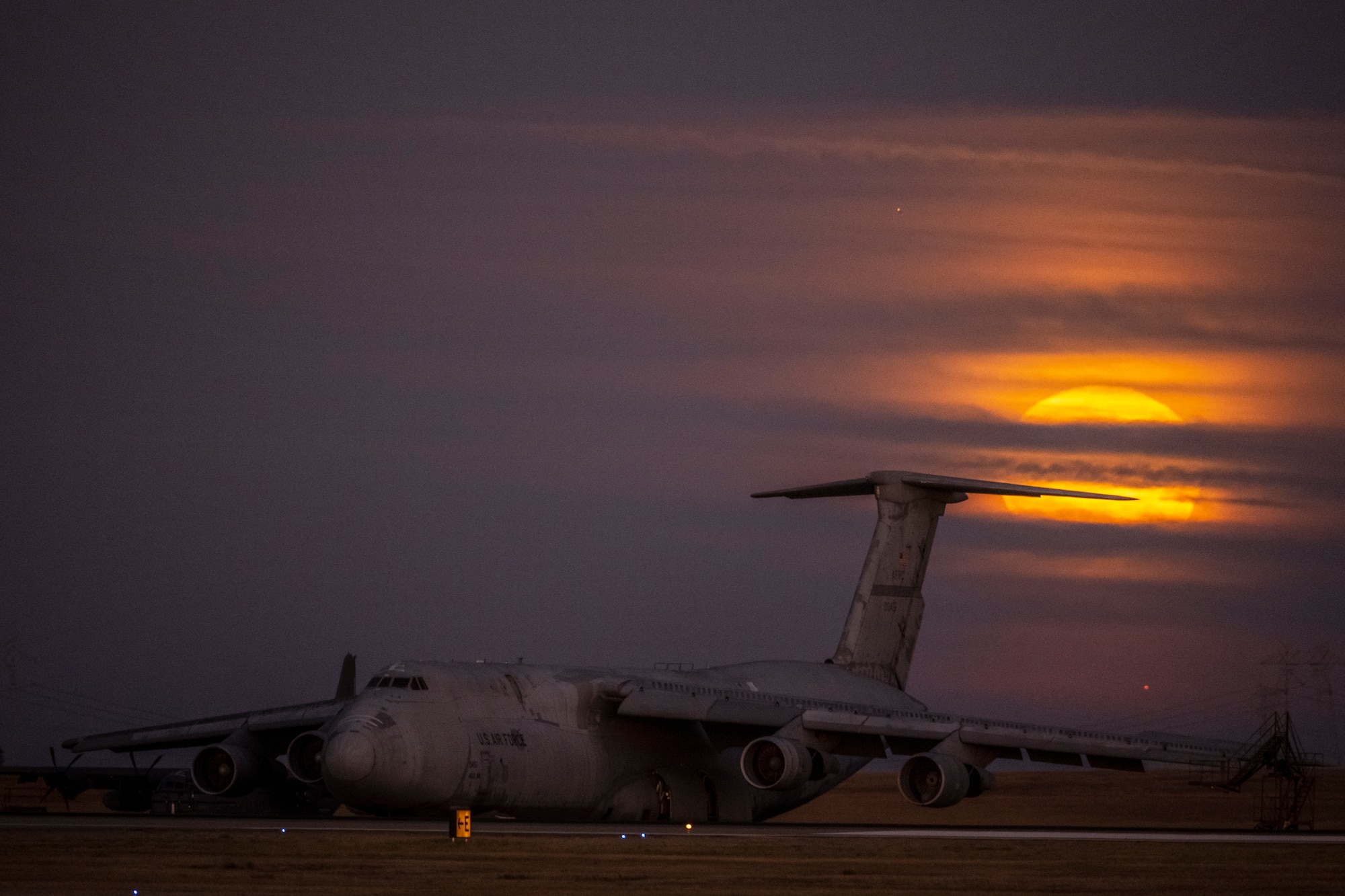 A large military aircraft sits under a large, bright orange moon.