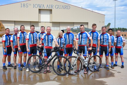 Group of cyclists pose for a photo in front of two fighter jets
