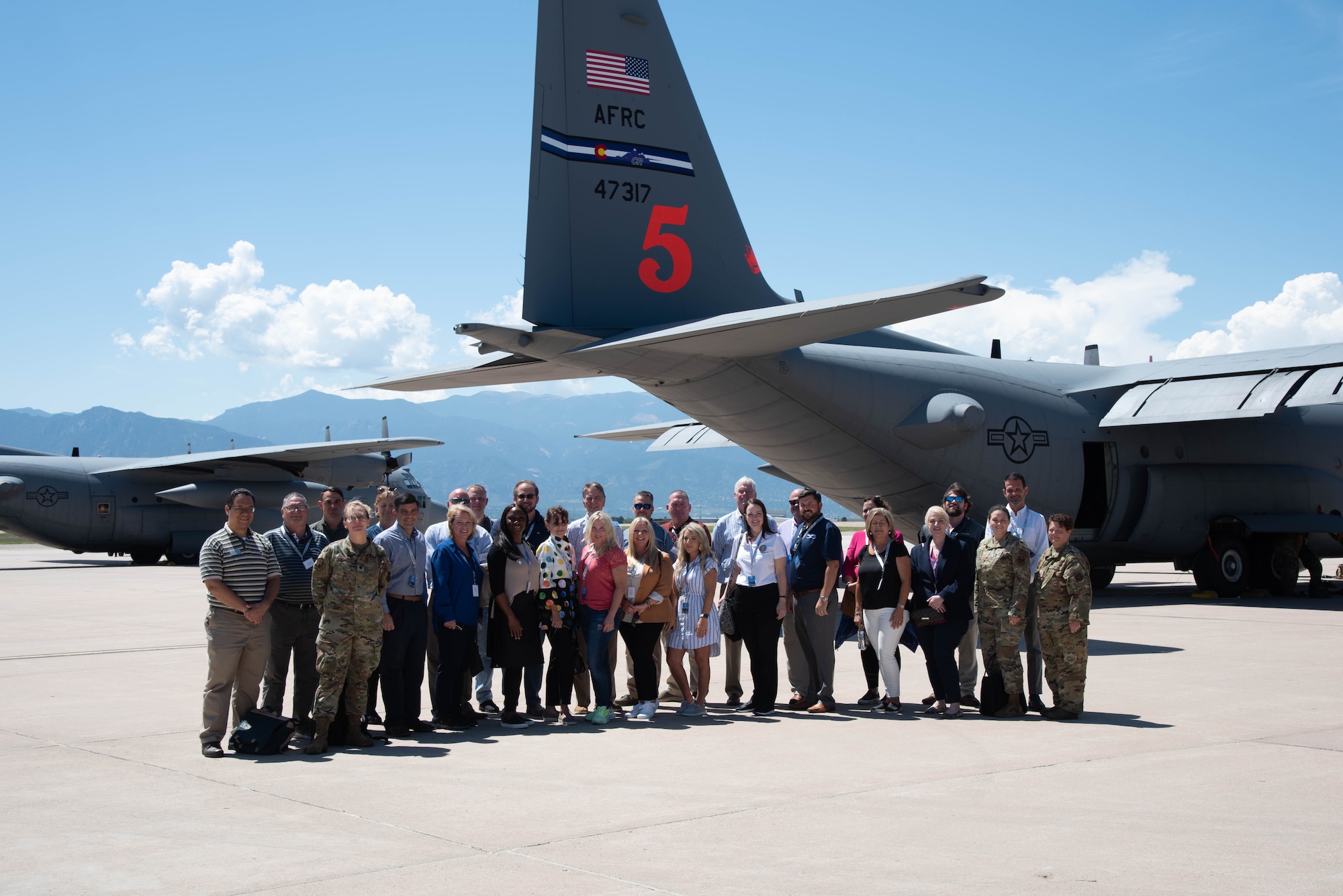 A group of civilians and Airmen stand in front of a C-130H tail