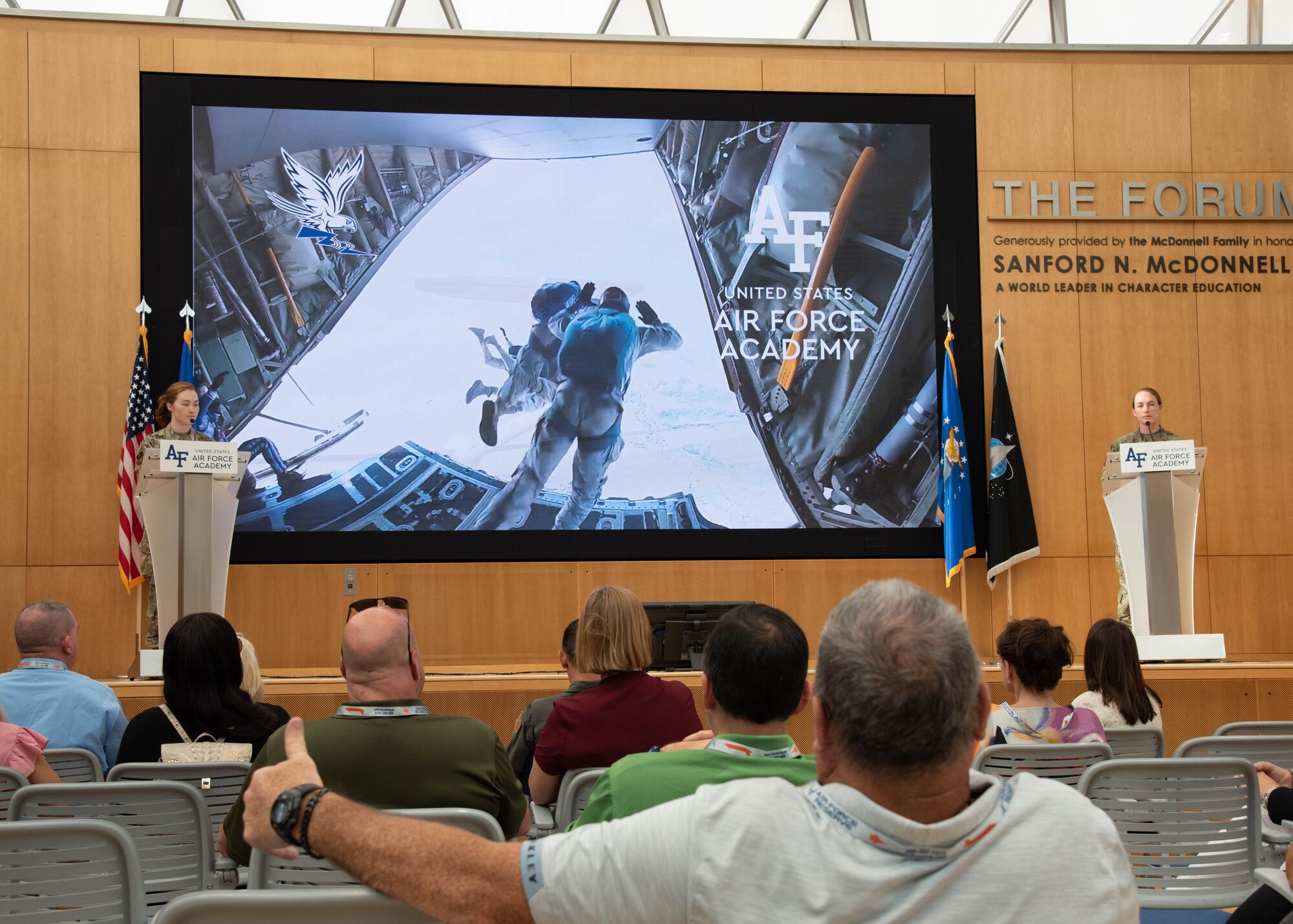 People sit in an auditorium looking at a screen and people onstage