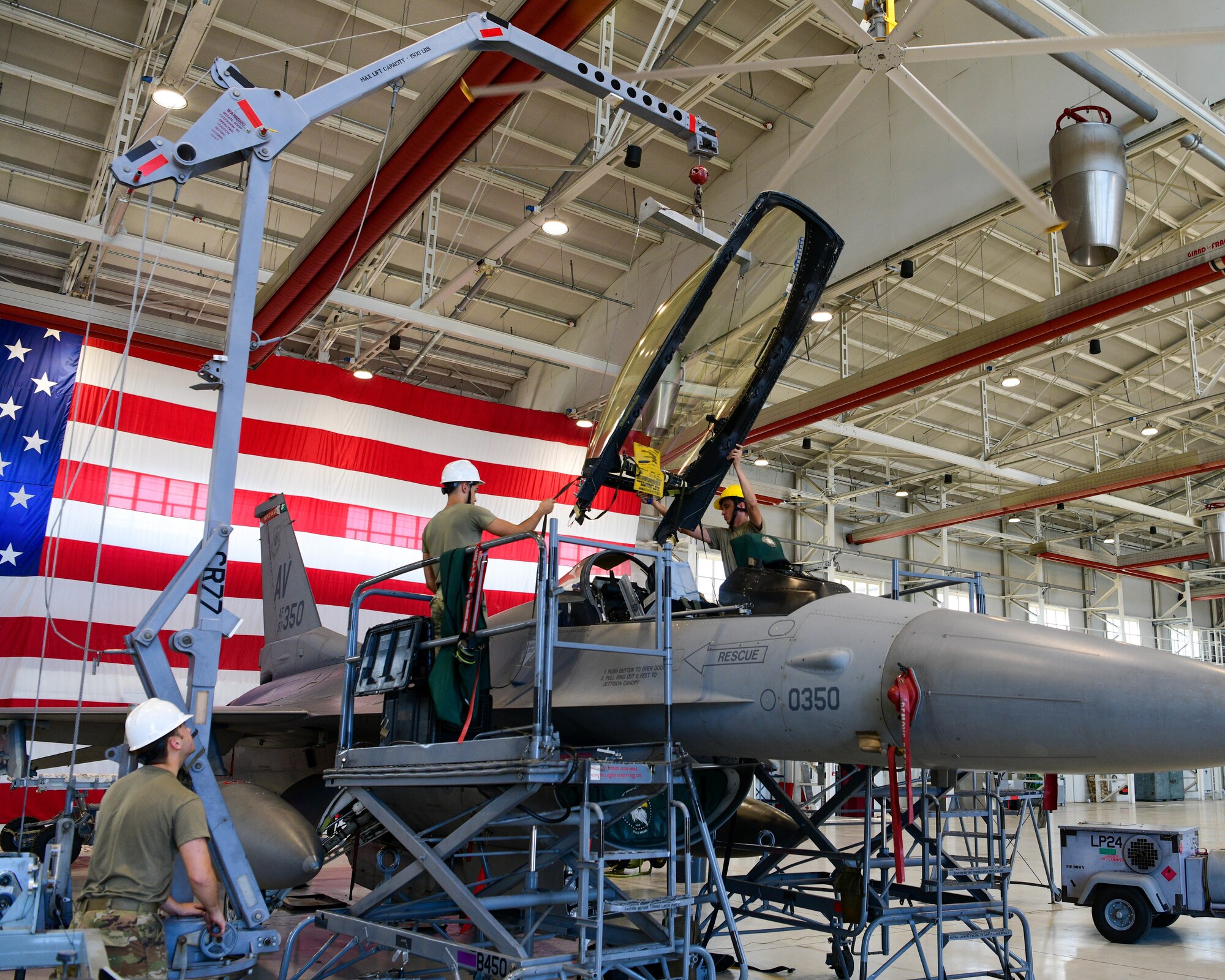 U.S. Air Force Airmen assigned to the 31st Maintenance Squadron Egress shop place a canopy onto an F-16 Fighting Falcon at Aviano Air Base, Italy, Aug. 11, 2022. Aviano was chosen as one of six bases across multiple major commands that have different environmental factors to test a new Luna transparency for the F-16 canopy. (U.S. Air Force photo by Senior Airman Brooke Moeder)