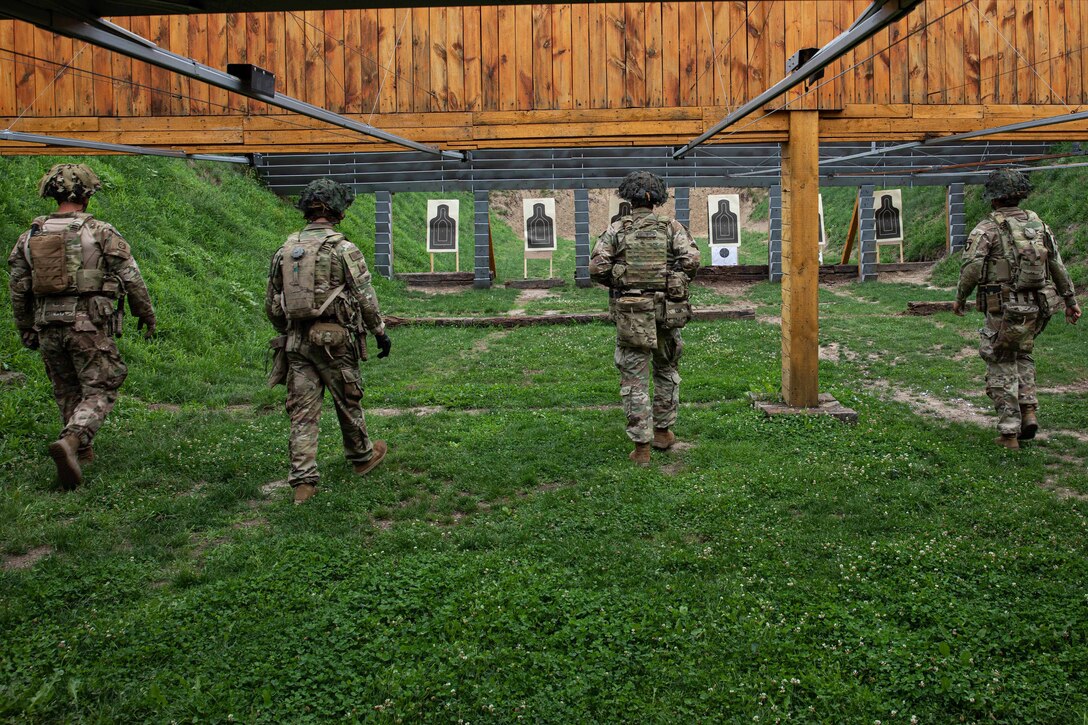 Four soldiers walk towards their targets at a shooting range.