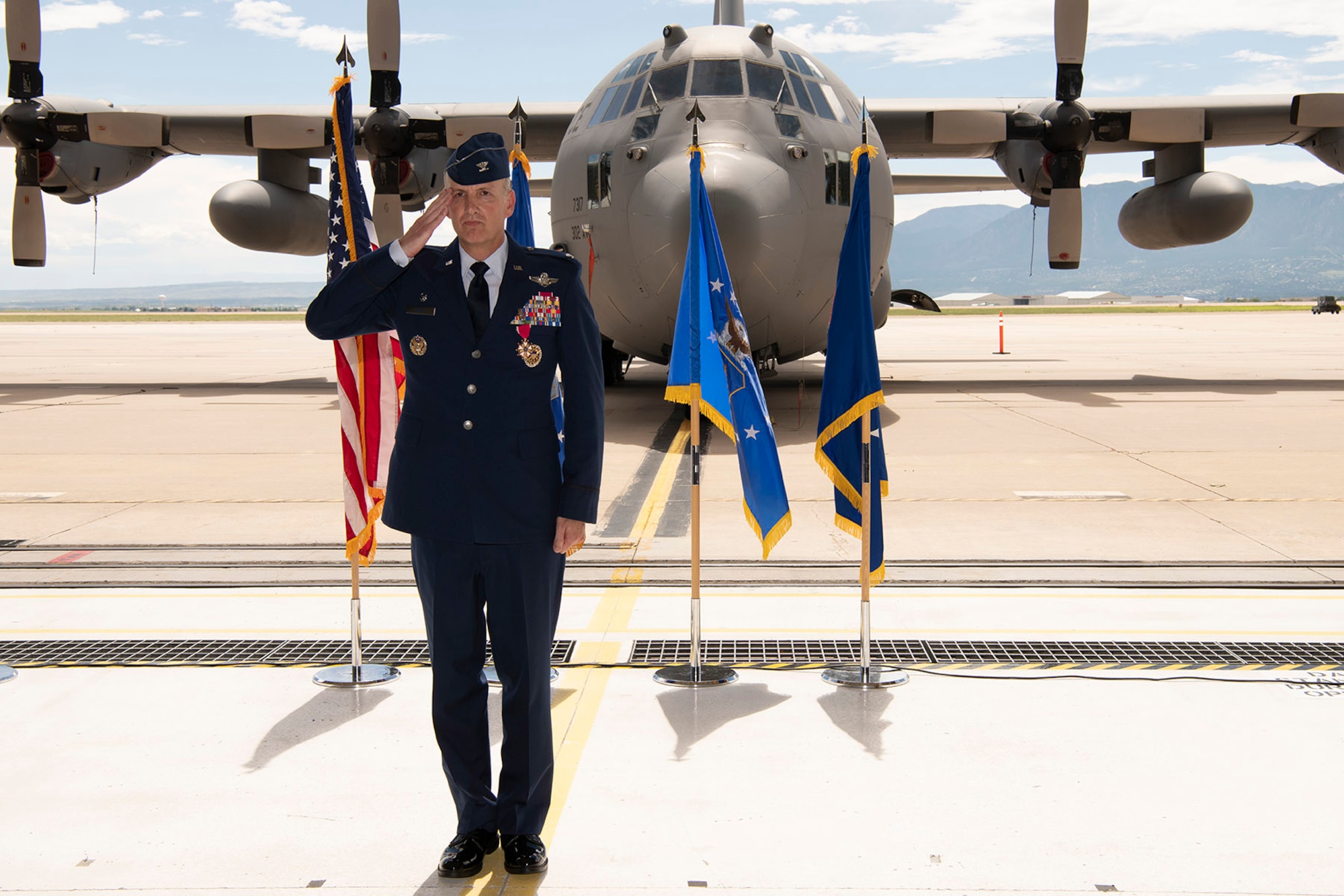 A man in Air Force service dress renders a salute with a C-130 in the background.