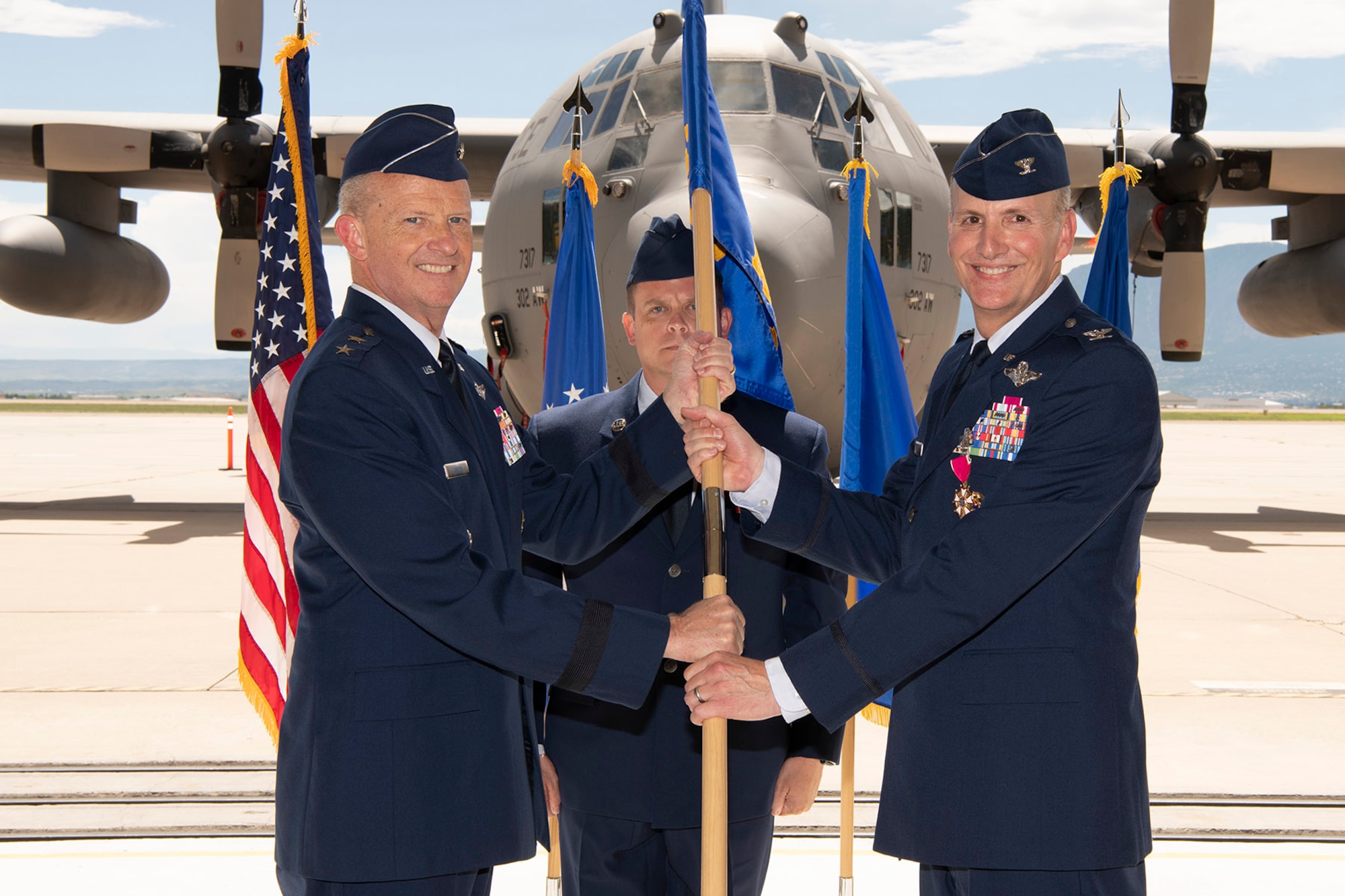 Three men in Air Force service dress stand with a blue guidon affixed to a flagstaff.