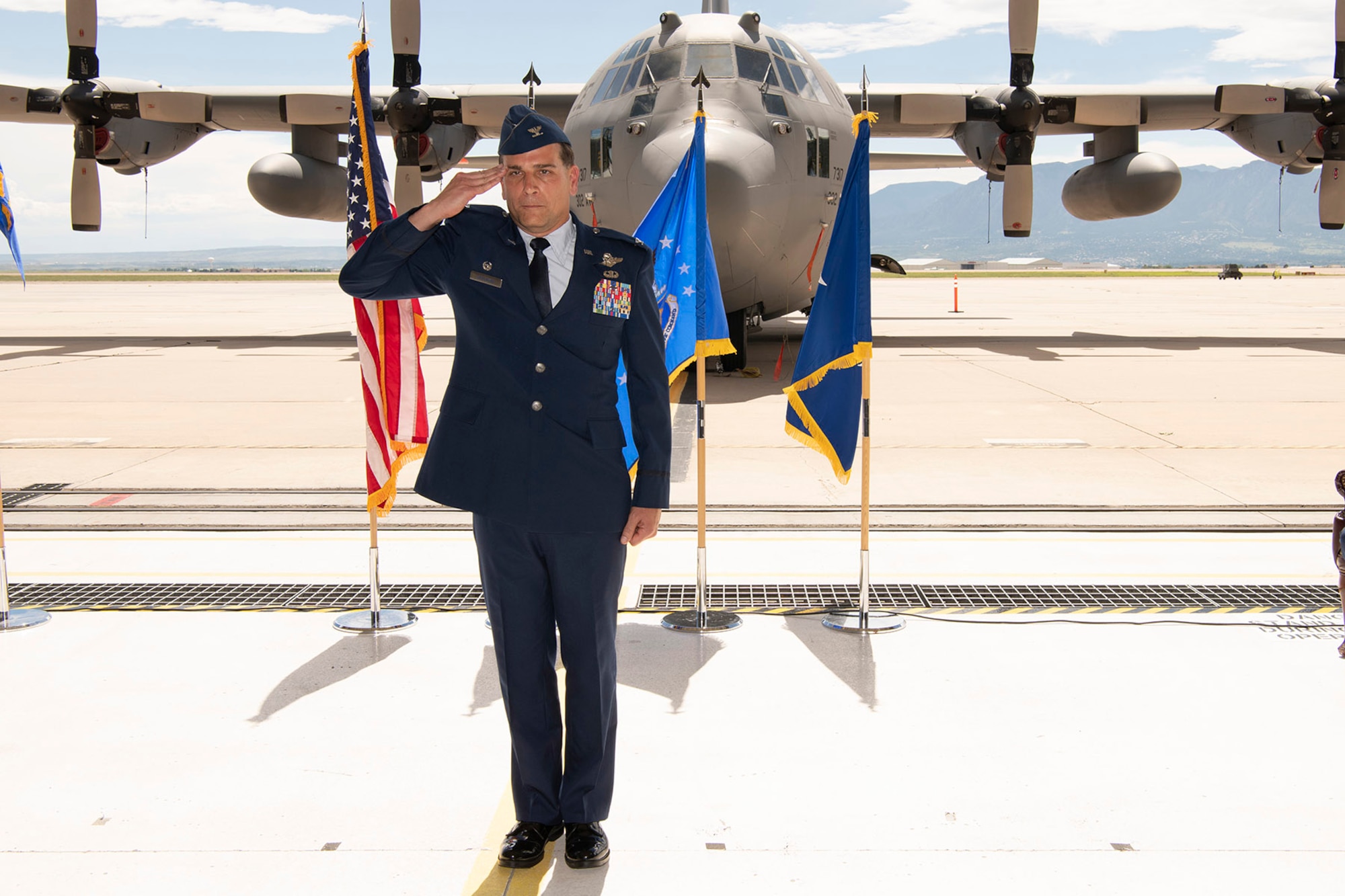 A man in Air Force service dress renders a salute with a C-130 in the background.