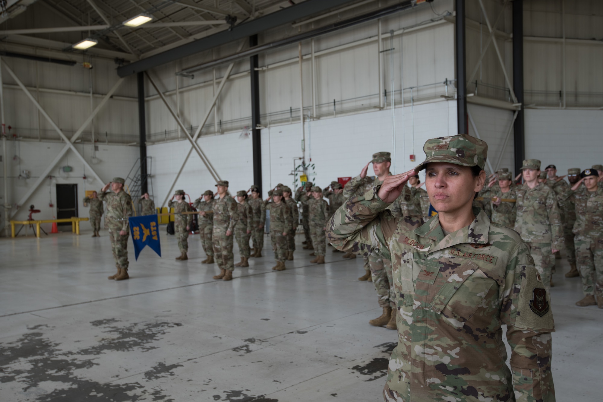 A woman in Air Force duty uniform leads other Airmen in a group salute.