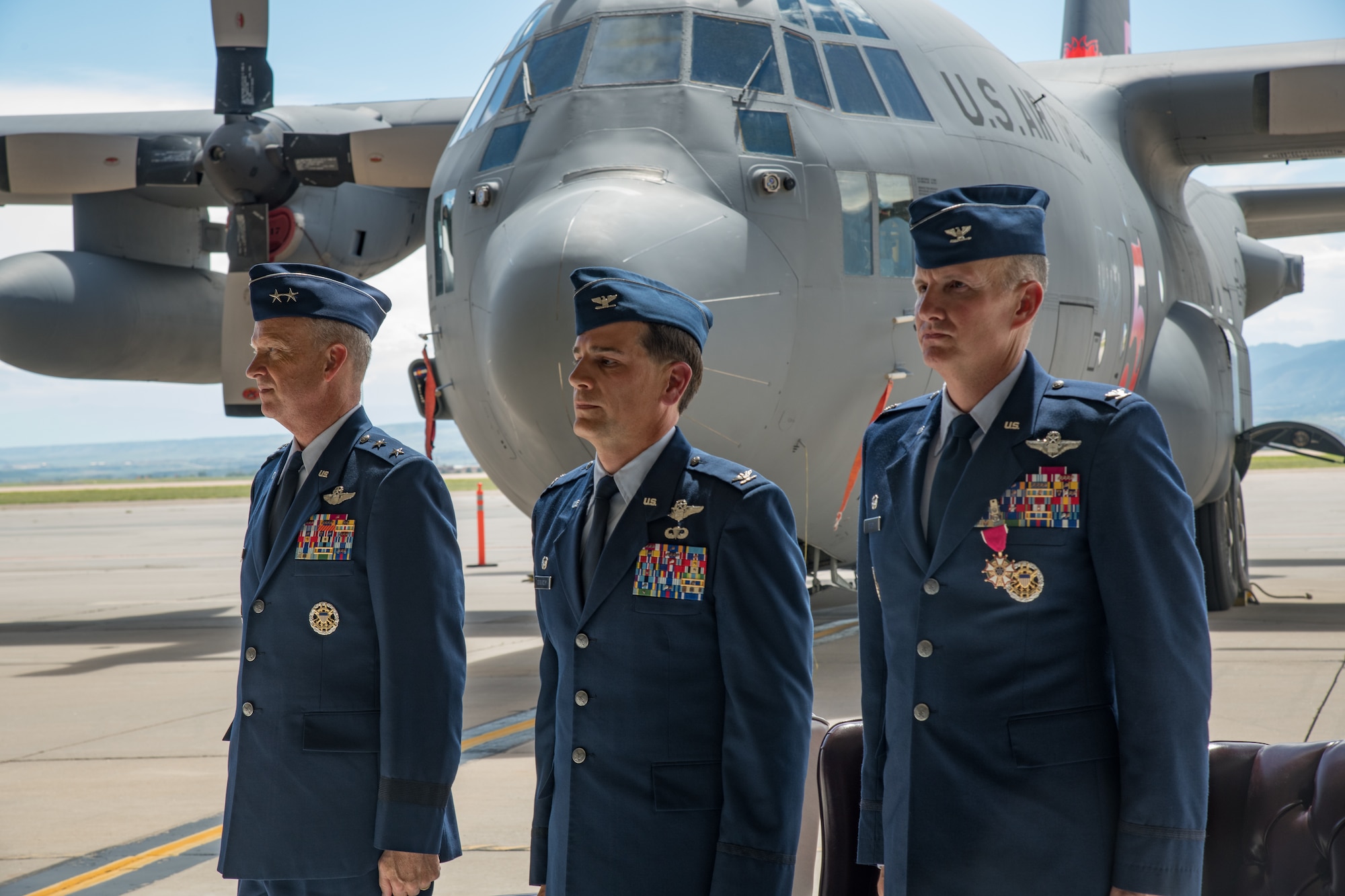 Three men in Air Force service dress stand together in front of a C-130.