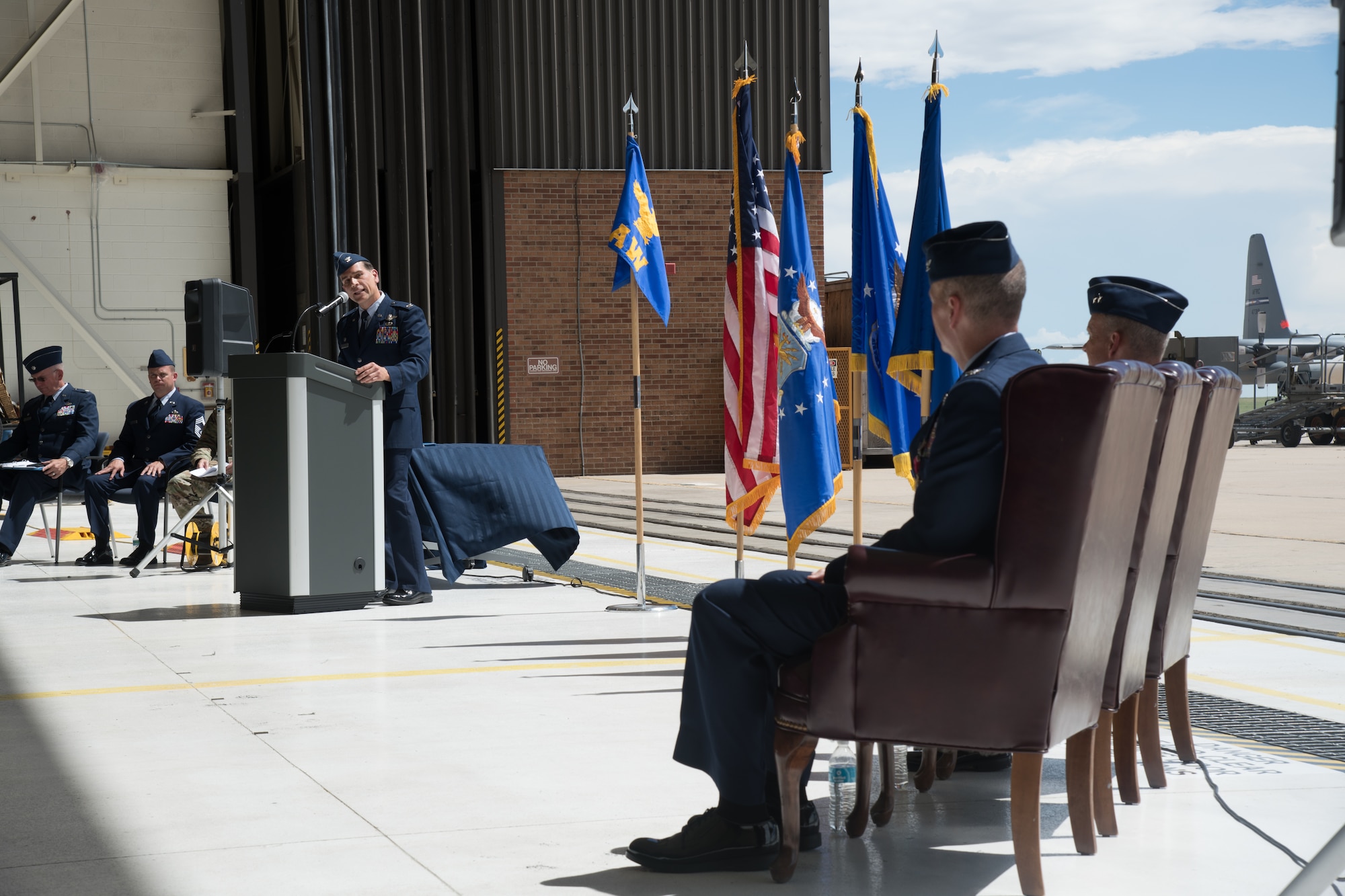 A man in Air Force service dress speaks to two men in Air Force service dress seated in chairs.