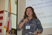 Lady of Korean decent with microphone tells members of the North Alabama Korean Association her personal story of how she chose a career with Huntsville Center during NAKA's celebration of Gwangbokjeol, also known as National Liberation Day in the Republic of South Korea.