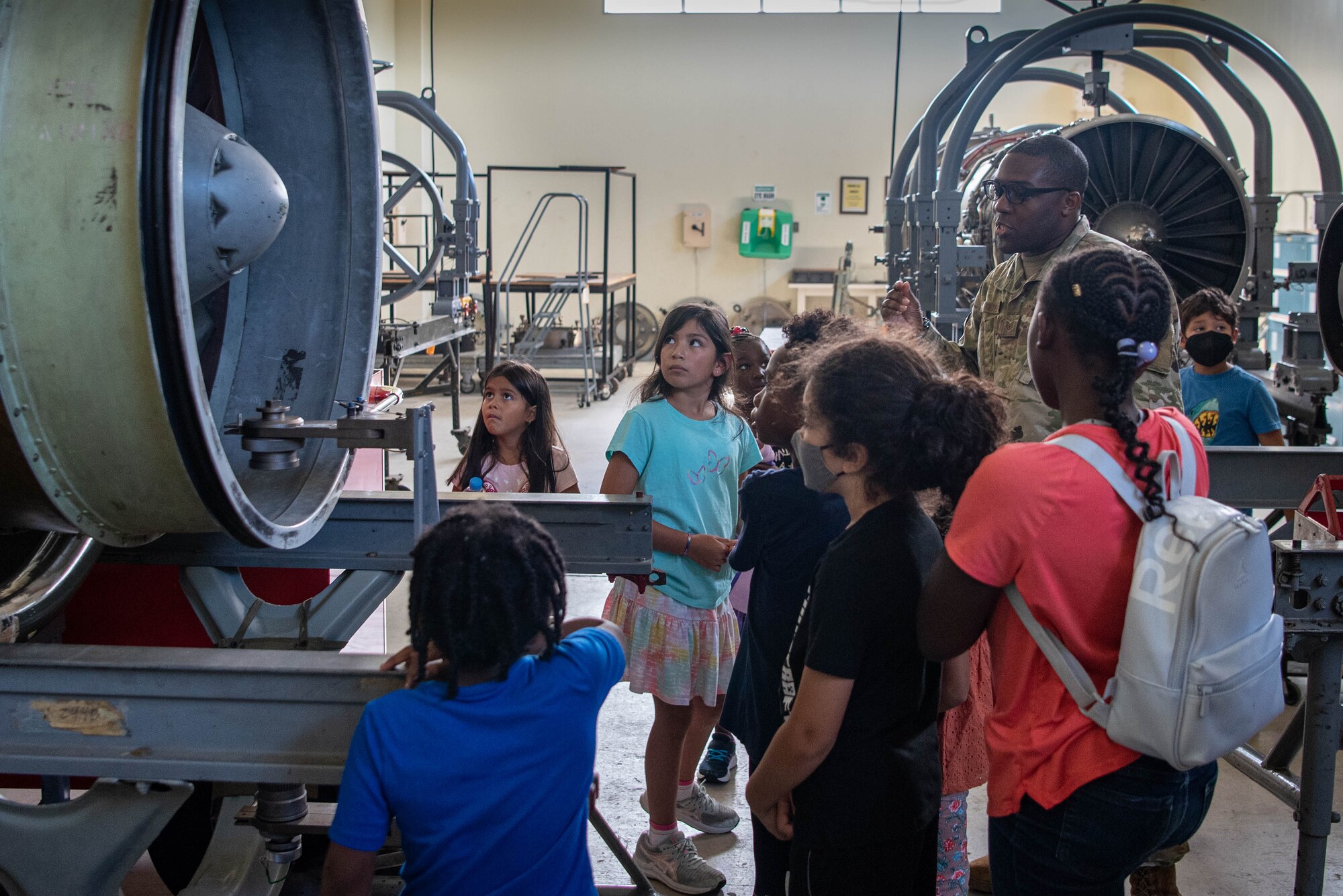 Students gather around an engine while an Airman gives a presentation.