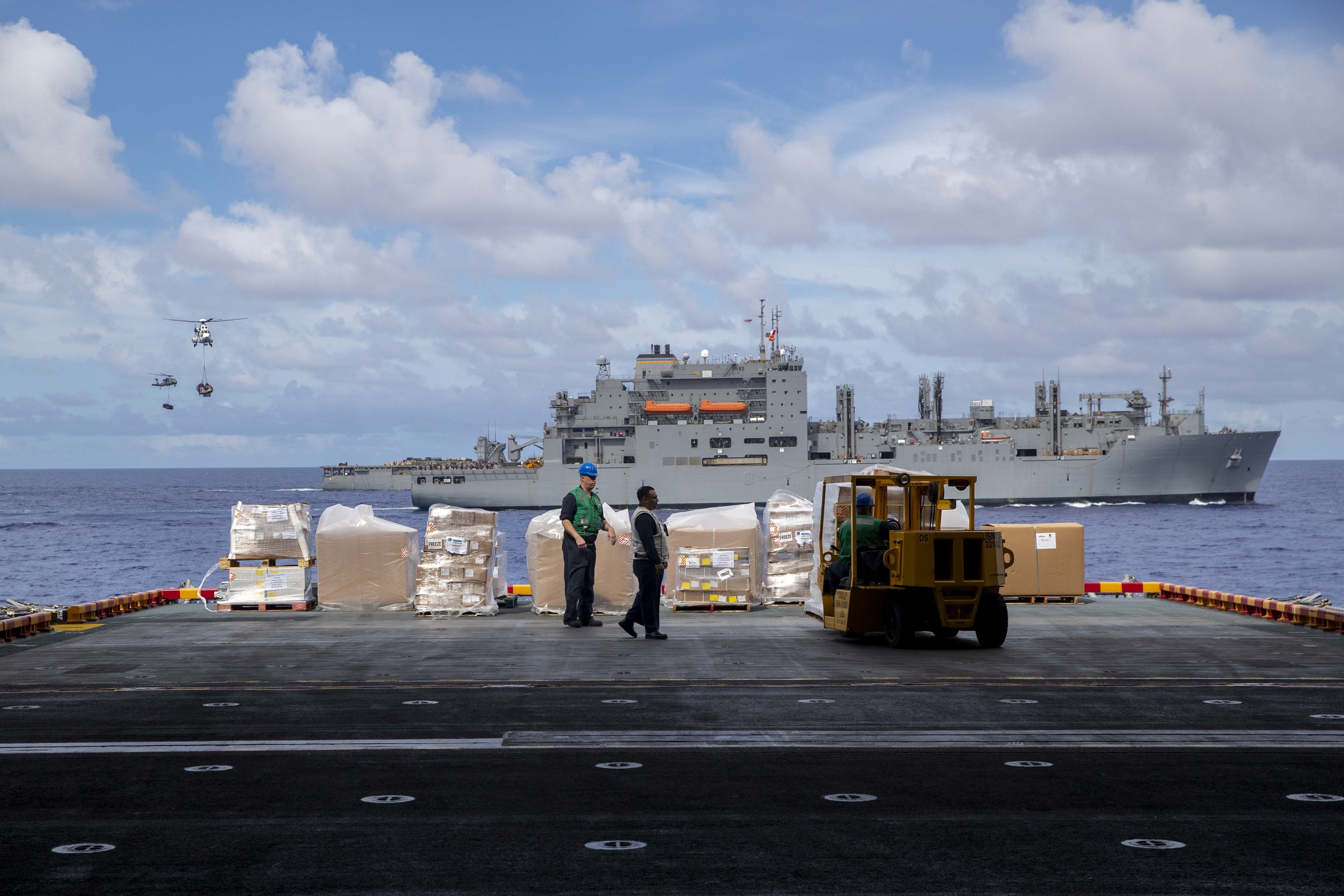 Sailors move supplies aboard USS Tripoli (LHA 7) during a vertical replenishment with USNS Carl Brashear (T-AKE 7).