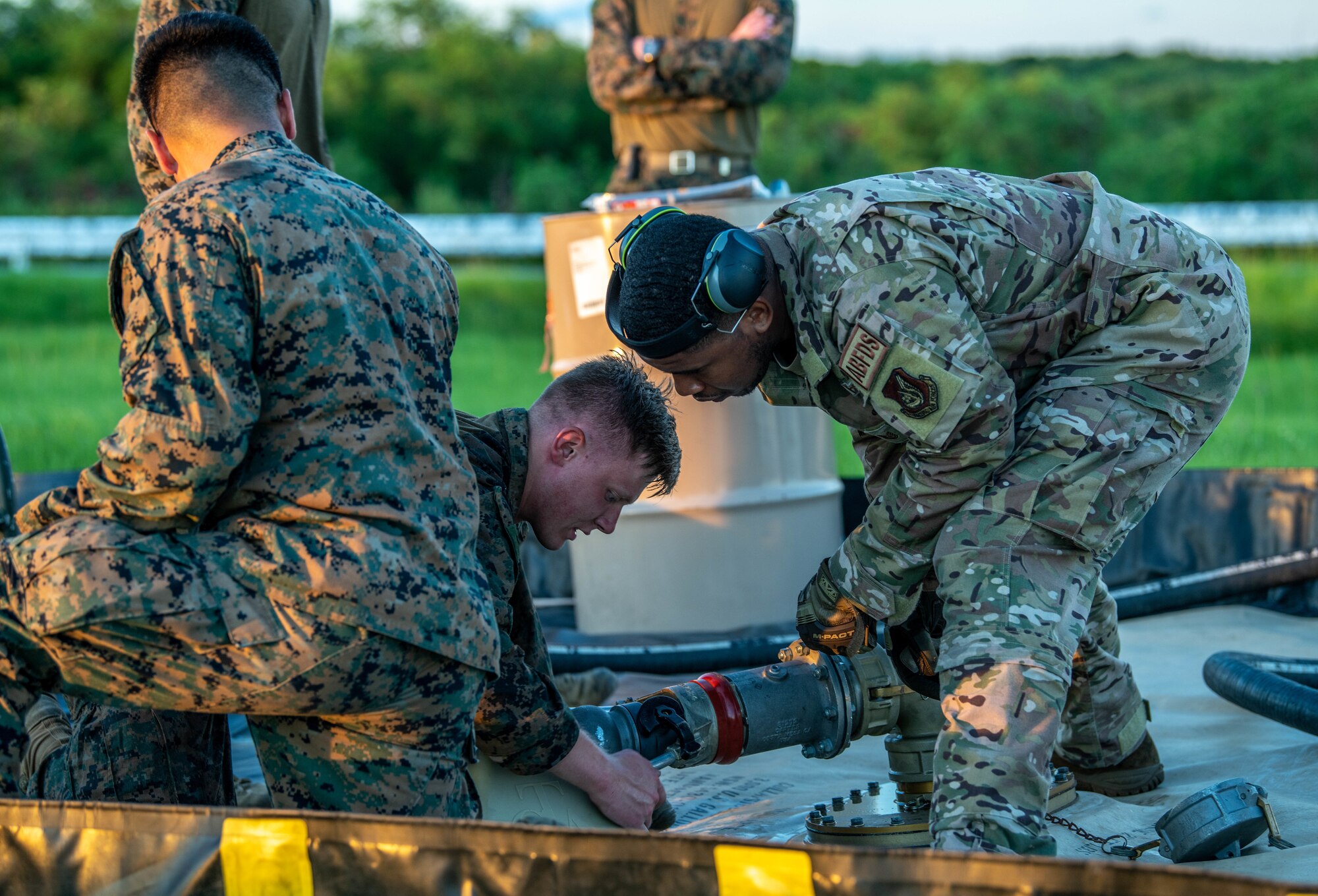 An Airman assists Marines with a forward aerial refueling point by guiding a fuel hose from an aerial bulk fuels delivery system to an empty fuel bladder