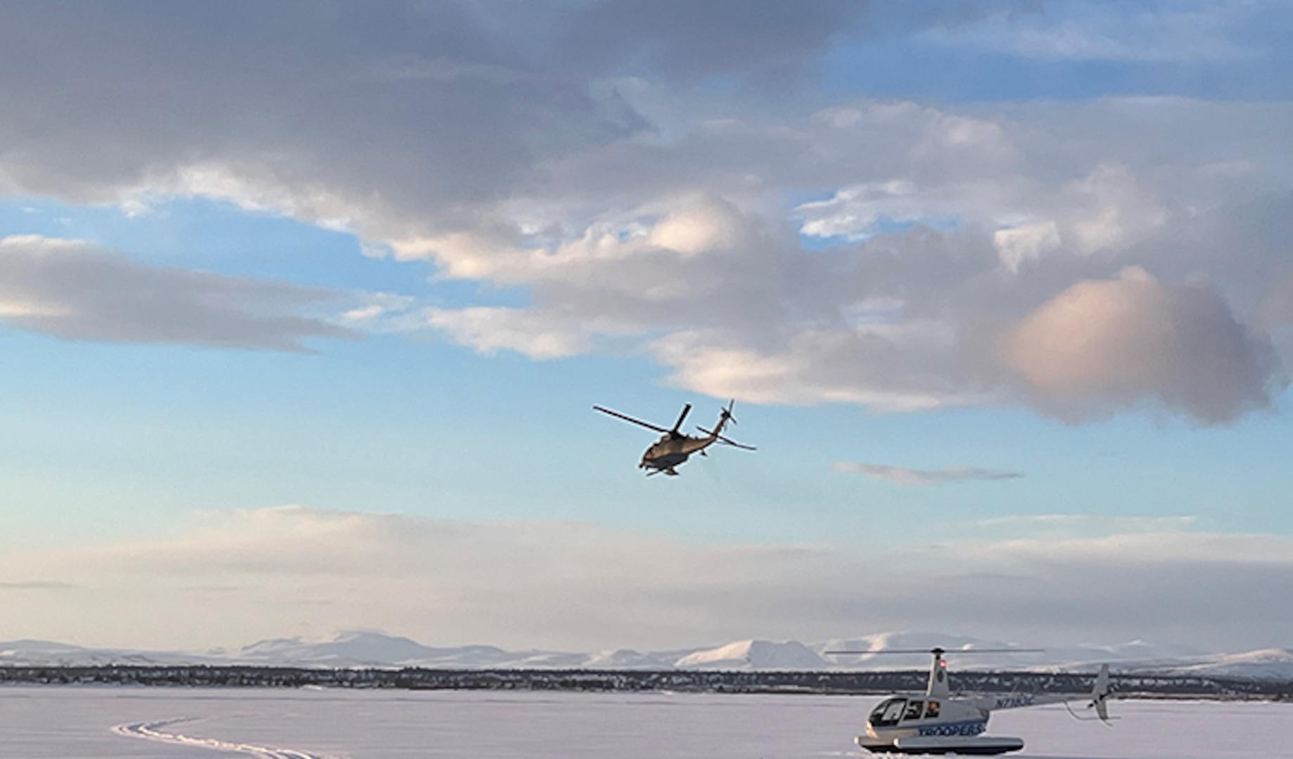 An airborne 210th Rescue Squadron HH-60G Pave Hawk conducts rescue operations March 5, 2022, at the Lake Iliamna crash site of a Cessna 206. The scope of the rescue effort was illustrated by an Alaska State Trooper R-44 helicopter.