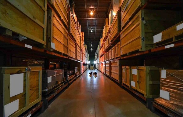 A view of one of the warehouse aisles where stacks and stacks of artifacts belonging to the National Cryptologic Museum stretch into the darkness beyond.