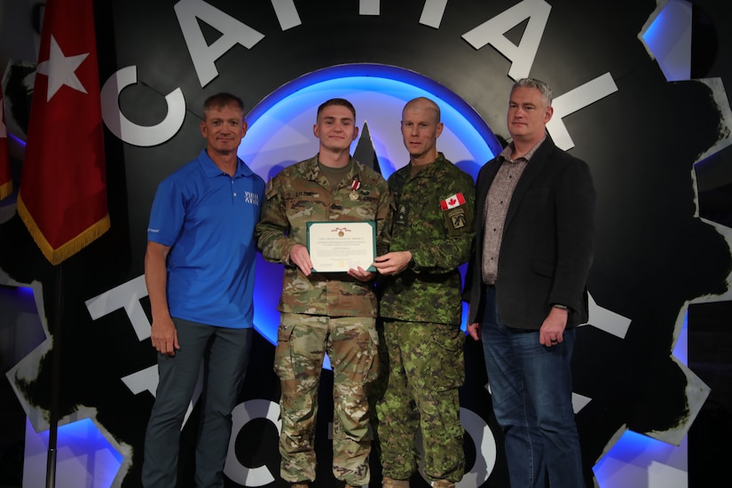 A man poses with an award while three other men stand beside him.