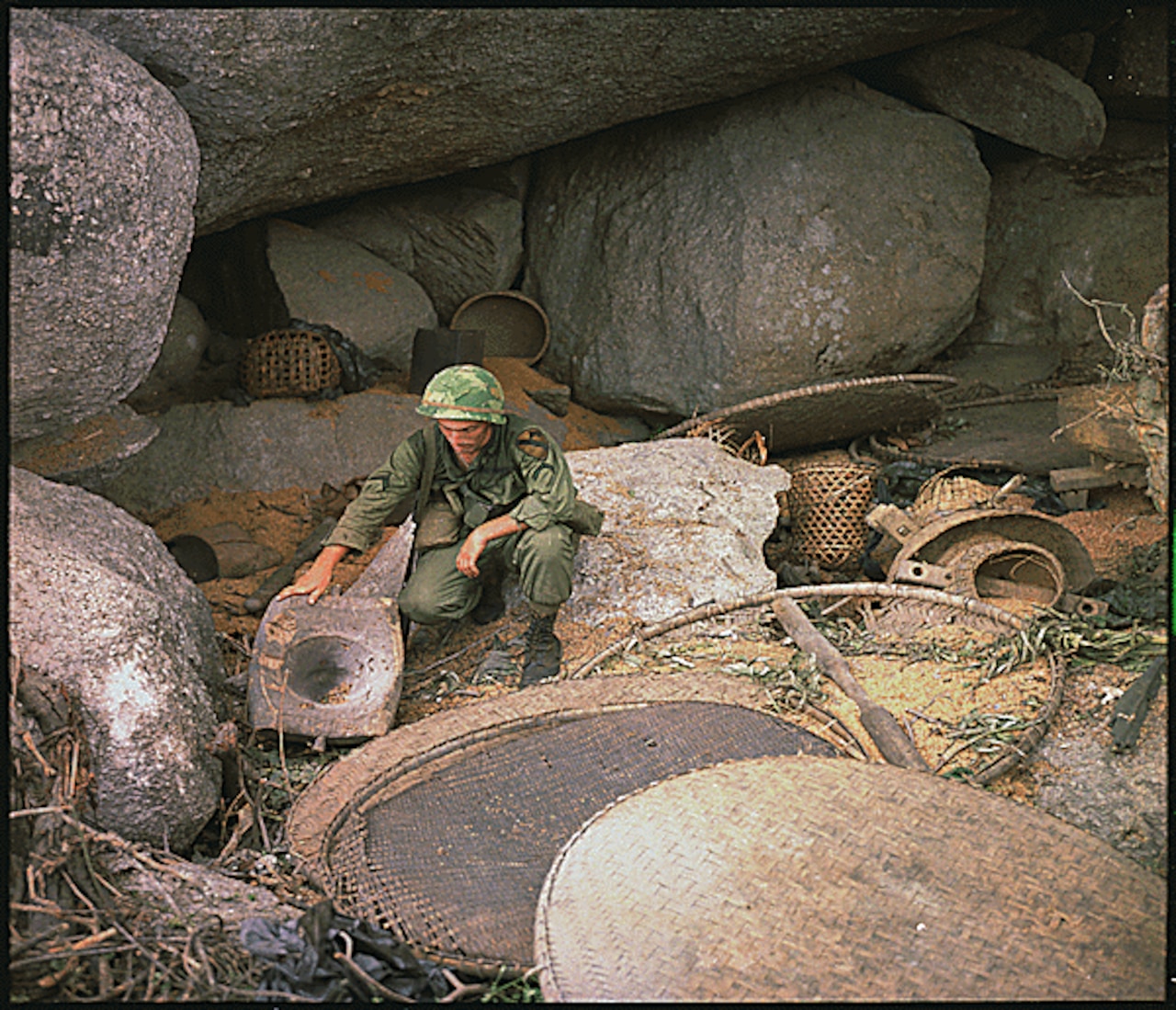 A crouching service members looks around a rock cave.