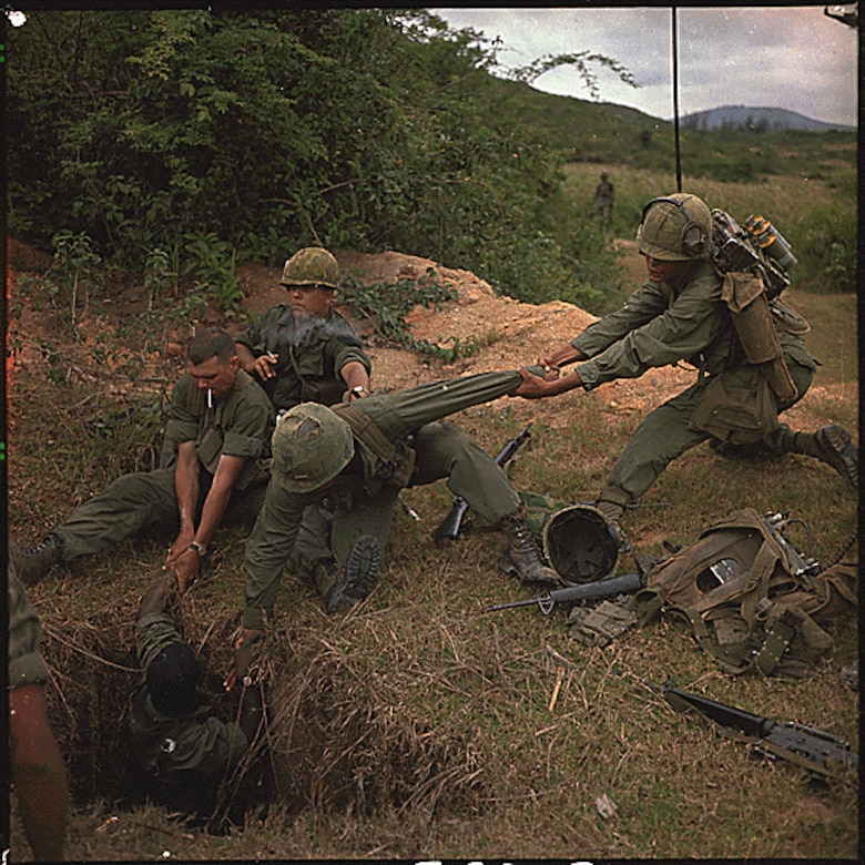 Four service members work to lower another service member into a deep tunnel.
