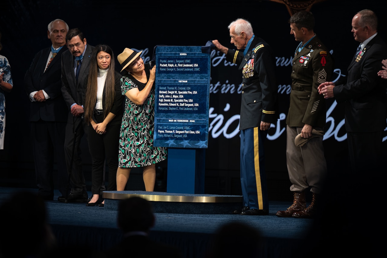 Seven people on a stage look at a large plaque.
